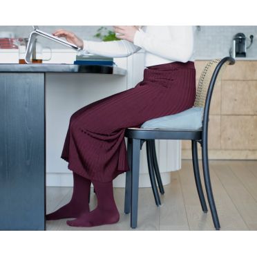 Kobieta siedzi przy stole na niebieskiej poduszce klinowej, wspierającej ergonomiczną pozycję.